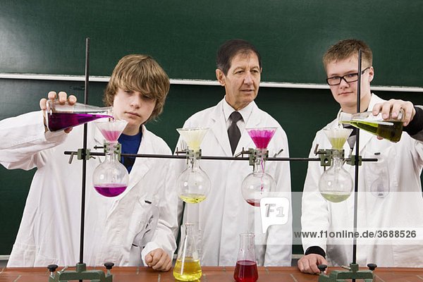 Ein Lehrer  der zwei Schüler betreut  die ein Chemie-Experiment durchführen.