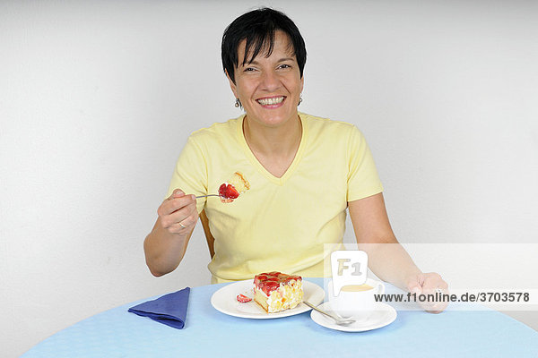 Frau sitzt am Tisch und genießt Kaffee und Kuchen