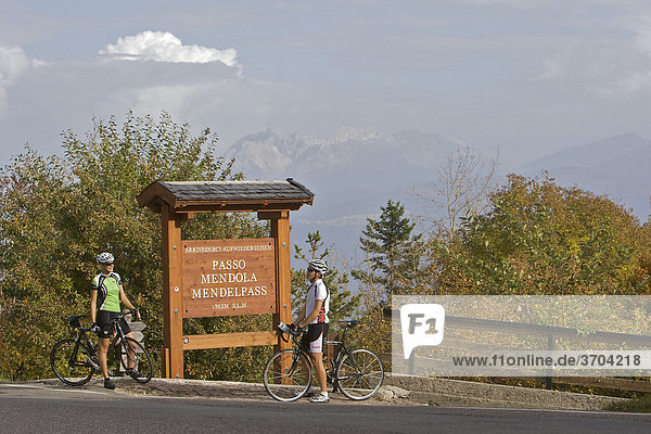 Rennrad-Fahrerin und Fahrer vor Schild am Mendel-Pass oberhalb von Kaltern  Südtirol  Italien  Europa