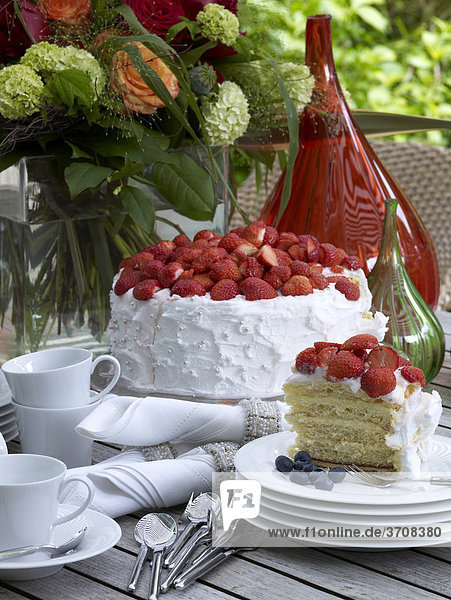 Sommerlicher Gartentisch mit Erdbeer-Sahnetorte auf weißem Porzellan
