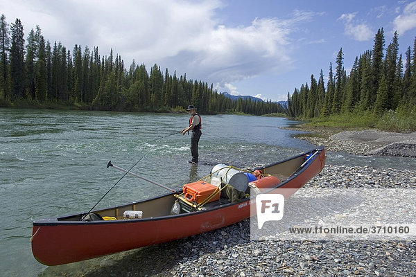 Kanu am Ufer des oberes Liard River Flusses  Kies  angelnder Mann dahinter  Yukon Territory  Kanada