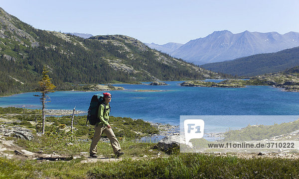 Young woman hiking  backpacking  hiker with backpack  historic Chilkoot Pass  Chilkoot Trail  Deep Lake behind  Yukon Territory  British Columbia  B. C.  Canada