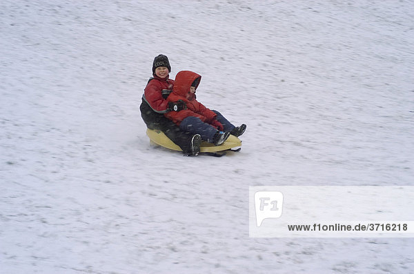 Zwei Jungen fahren auf Schlitten bob einen Schneehang hinab