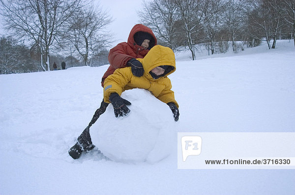 Two boys rolling big snowball