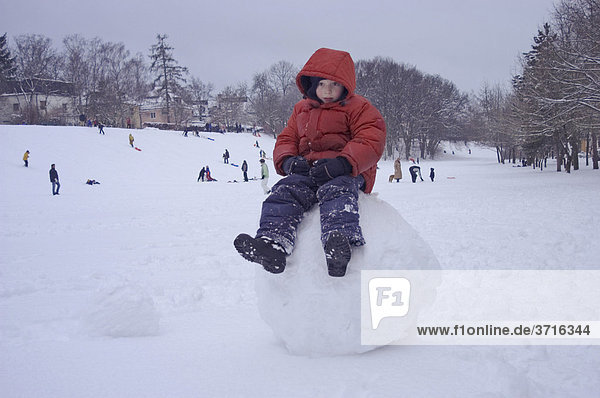 6-jähriger Junge sitzt auf großer Schneekugel