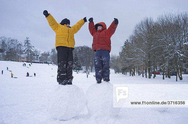 Zwei Jungen stehen auf großen Schneekugeln