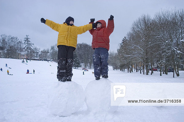 Two boys standing on big snoww balls