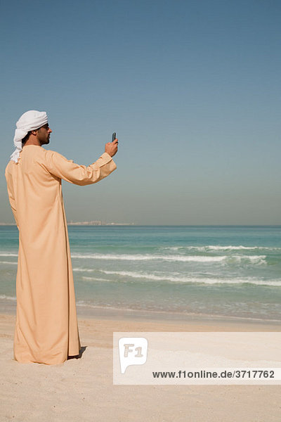 Mann aus dem Nahen Osten mit Handy am Strand