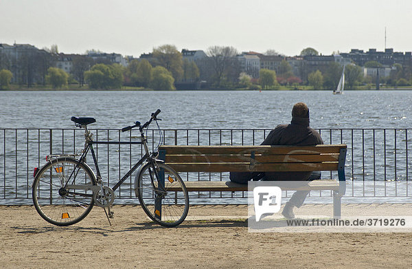 Ein Radfahrer macht eine Pause auf einer Bank an der Außenalster in Hamburg