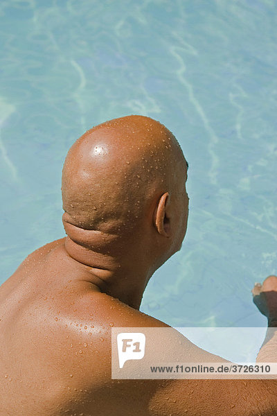 Glatzköpfiger Senior sitzt am Rande eines Swimmingpools
