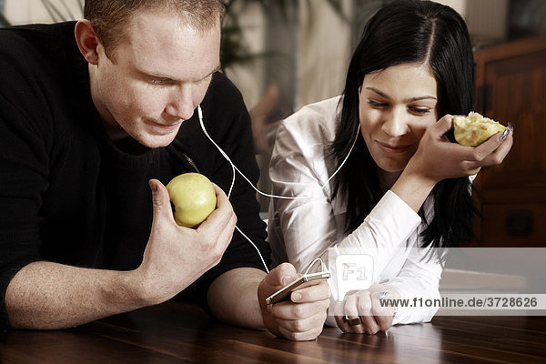 Young couple listening to music together and eating an apple