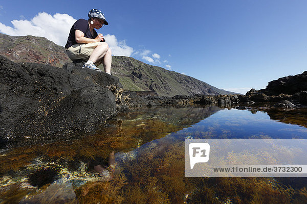 Woman sitting on a rock pool of a rocky coast  Paisaje protegido del Remo Nature Reserve  La Palma  Canary Islands  Spain