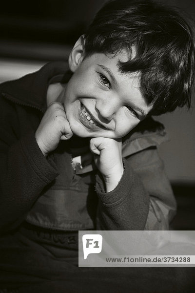 Small boy sitting on the floor heads leaning on his hands smiling cheekily