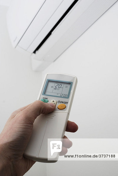 Hand adjusting the settings of a wall-mounted air conditioning unit with remote control