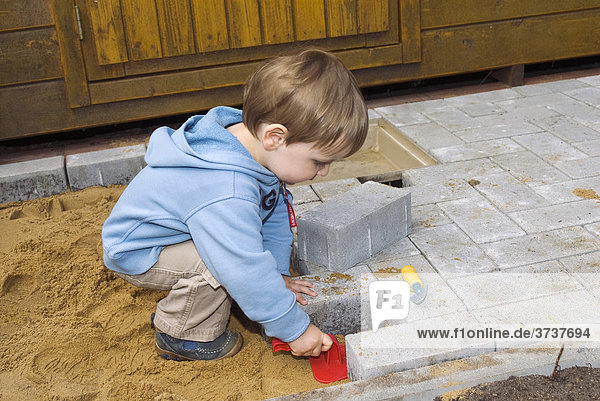 Kleiner Baumeister  ein kleiner Junge  20 Monate  hilft beim Pflastern einer Terrasse