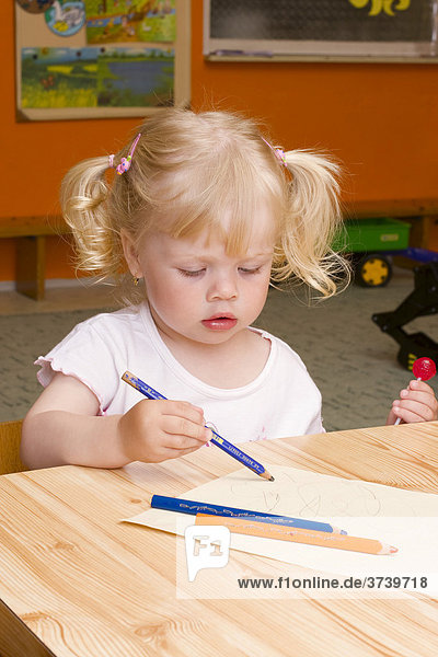 Two year old blond girl sitting at a table with coloring pencils