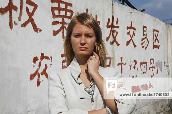 Young woman in front of a wall with chinese lettering on it