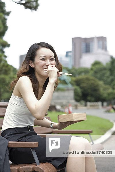 Young woman laughing while eating lunch in a park  Tokyo  Japan  Asia