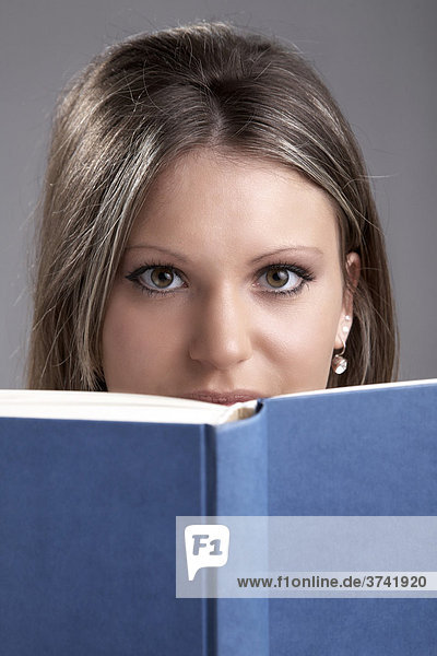Junge Frau sieht über ein blaues Buch in Richtung Kamera
