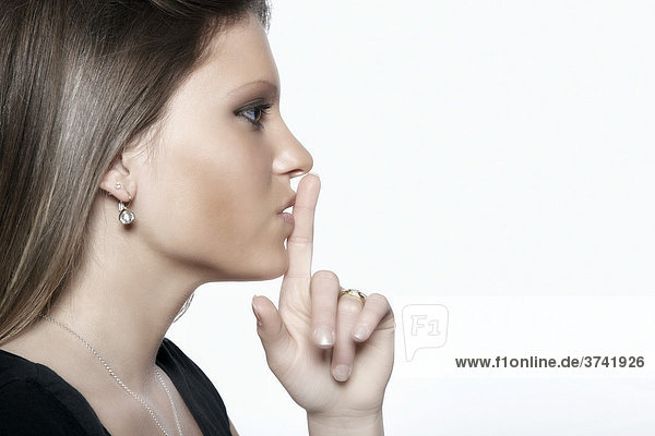 Young woman holding her index finger in front of her mouth asking for silence