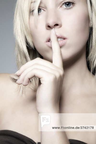 Junge blondhaarige Frau hält sich Zeigefinger vor den Mund  Portrait mund