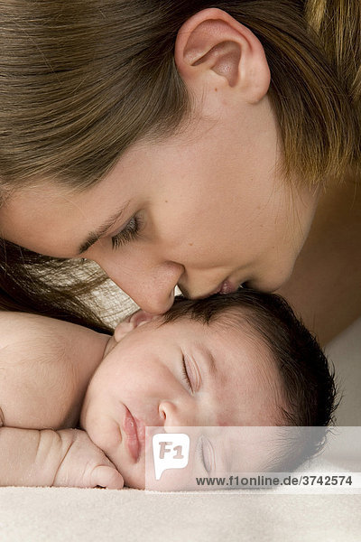 Mutter küsst ihr schlafendes neugeborenes Baby  zwei Wochen alt