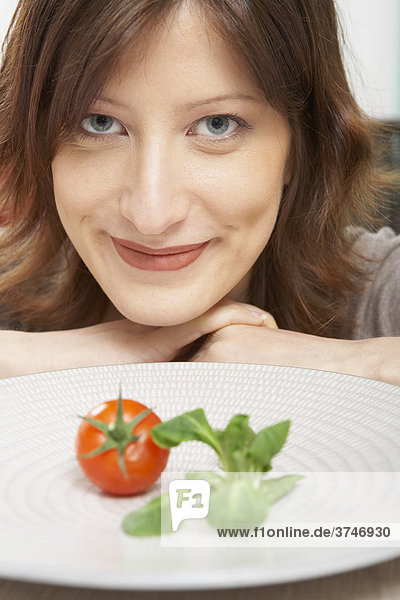 Junge Frau mit einzelner Tomate und Salat auf ihrem Teller