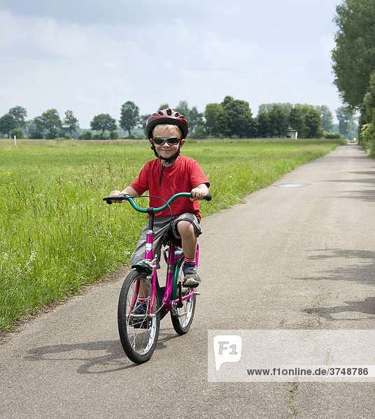 Ein Junge  vier Jahre  fährt Rad auf einer landwirtschaftlichen Straße