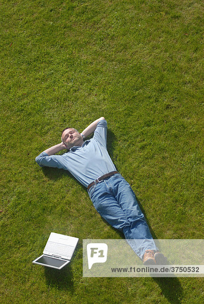 Zufriedener Mann entspannt sich auf dem Rasen mit PC