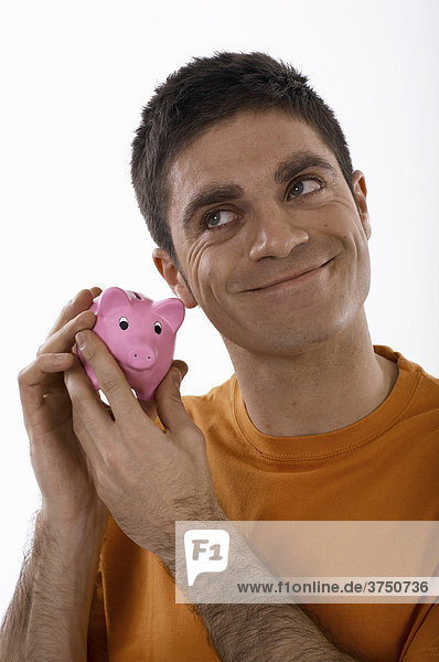 Smiling man holding a piggybank up to his ear