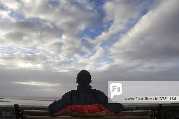 Mann sitzt auf Bank und schaut in Wolkenhimmel