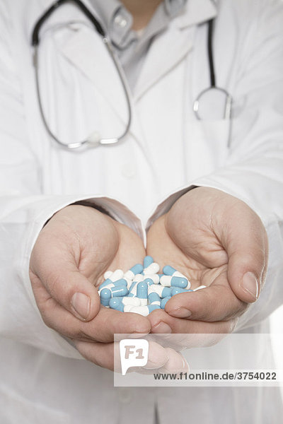 Arzt mit Stethoskop hält eine Hand voll Tabletten nach vorn