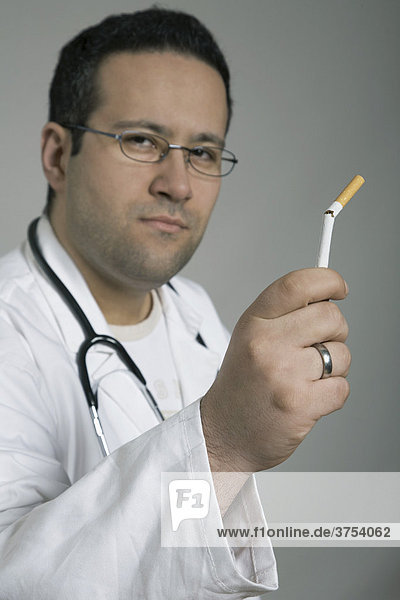 Arzt mit Stetoskop hält zerbrochene Zigarette in die Kamera