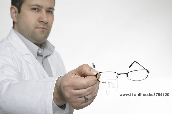 Augenarzt hält Brille in Richtung Kamera