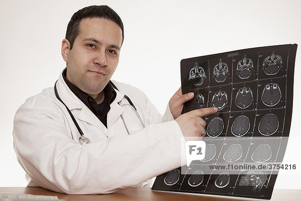 Arzt mit Stethoskop zeigt auf CT Aufnahmen eines Schädels