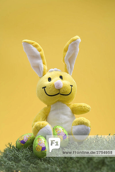 Yellow plush Easter bunny sitting in the grass with chocolate eggs