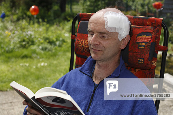 Mann mit Kopfverband sitzt in Gartenstuhl und liest Buch  45 Jahre  Geretsried  Bayern  Deutschland  Europa
