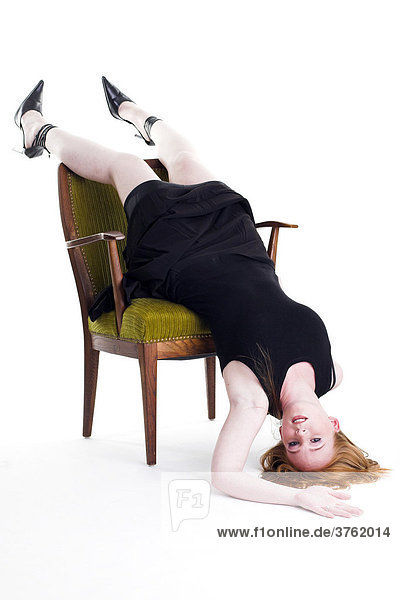 Eine rothaarige junge Frau liegt kopfüber auf einem Polsterstuhl