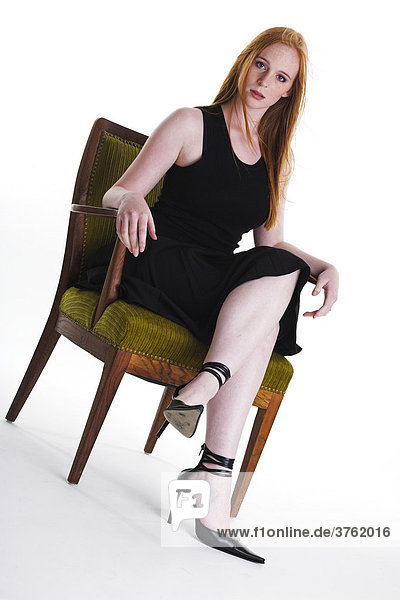 Eine rothaarige junge Frau sitzt auf einem Polsterstuhl