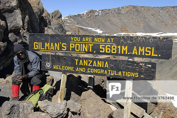 Einheimischer Führer am Schild auf dem Gipfel Gilman's Point (5681 m) Kraterrand Kilimandscharo Tansania