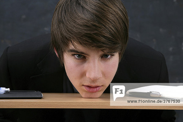 Junger Mann stützt Kopf auf Schreibtisch