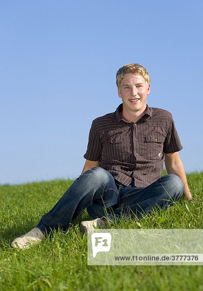 A young man sitting on a meadow