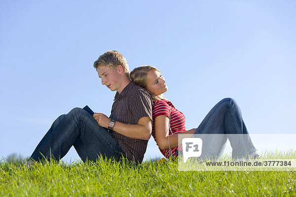 A young couple on a meadow  she is listening to music  he is reading a book