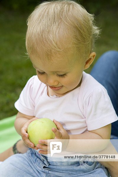 Ein 10 Monate altes Baby spielt mit einem Apfel