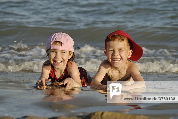 Zwei Kinder liegen am Strand im Wasser und freuen sich