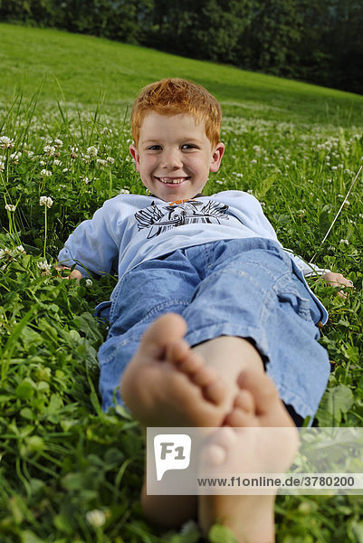 Junge liegt barfuss in einer Blumenwiese