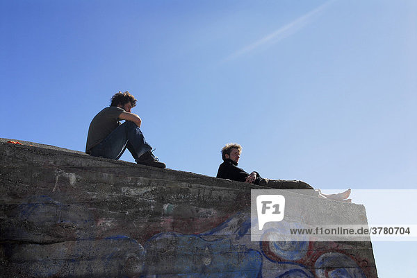 Zwei junge Männer sitzen auf einer Mauer und geniessen die Sonne