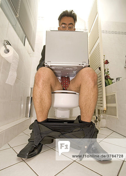 Verrückter Geschäftsmann mit Notebook auf der Toilette