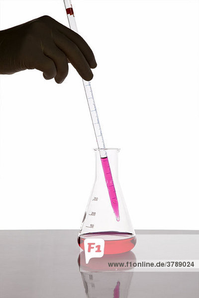 Ein Laborant  der mit einem Tropfer Flüssigkeit in ein Becherglas gibt.
