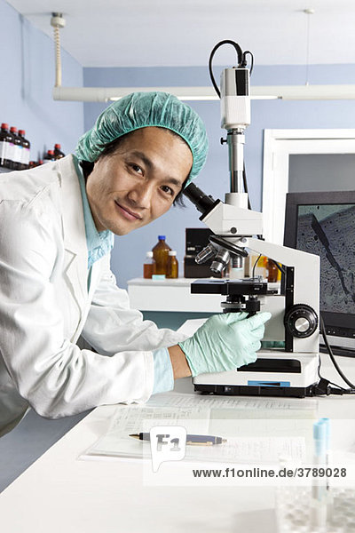 A lab technician using a microscope  looking at camera